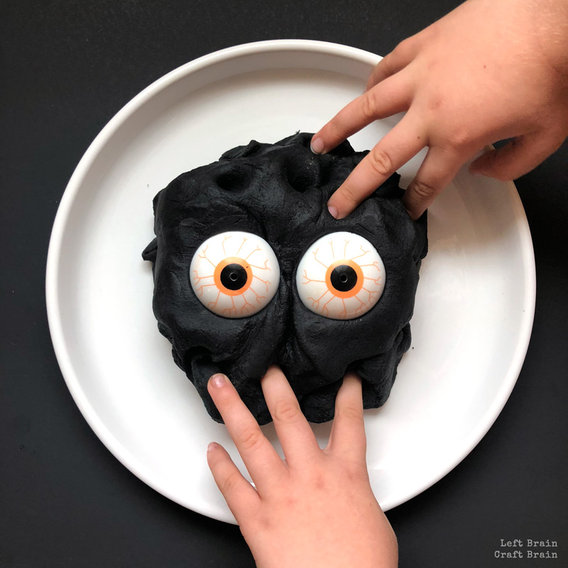 black playdough with monster eyes and hands playing in it