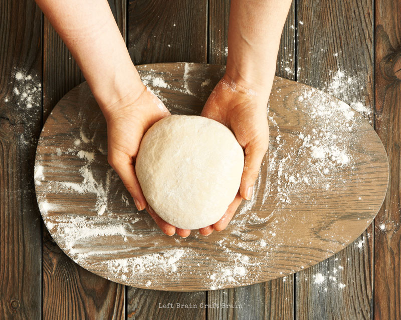 bread dough in a ball in hands over a floury wooden board and counter