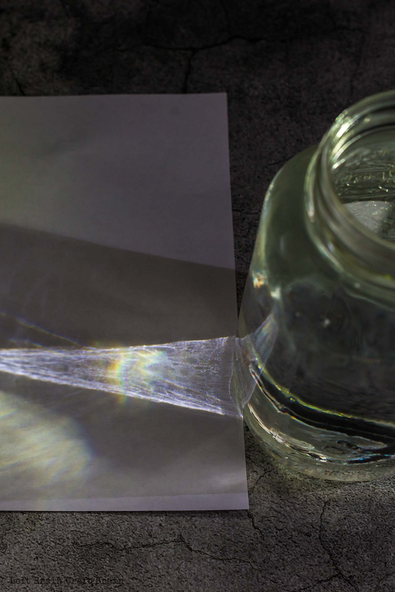 jar of water in dark with flashlight beam and rainbow on paper