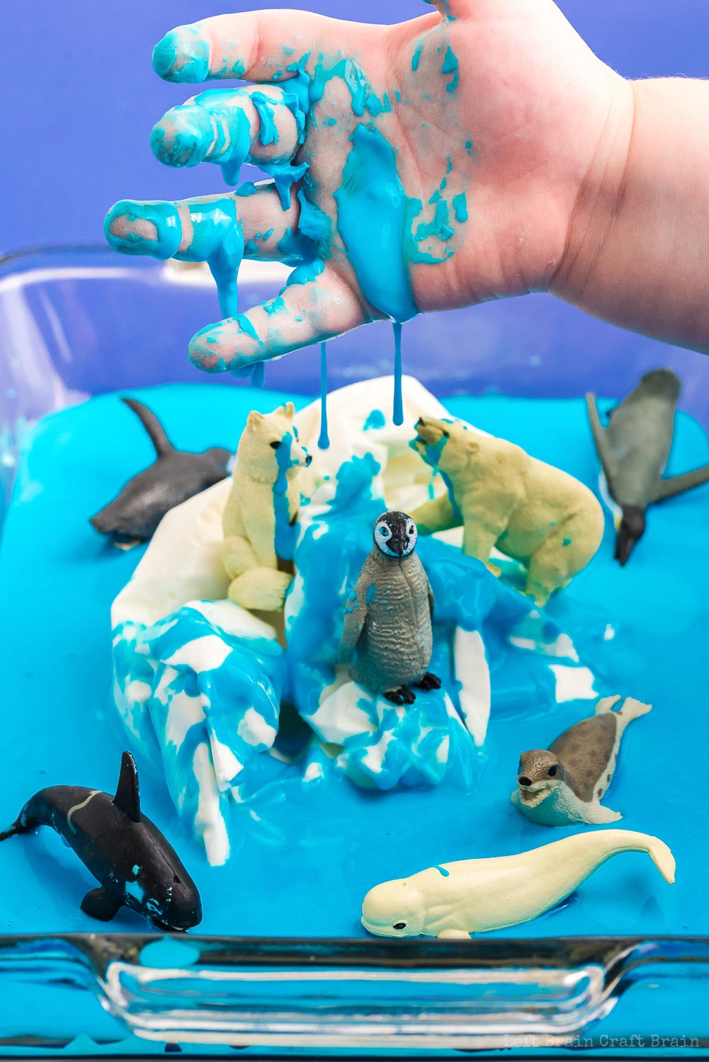 messy hand with blue oobleck over frozen oobleck iceberg with polar animal toys